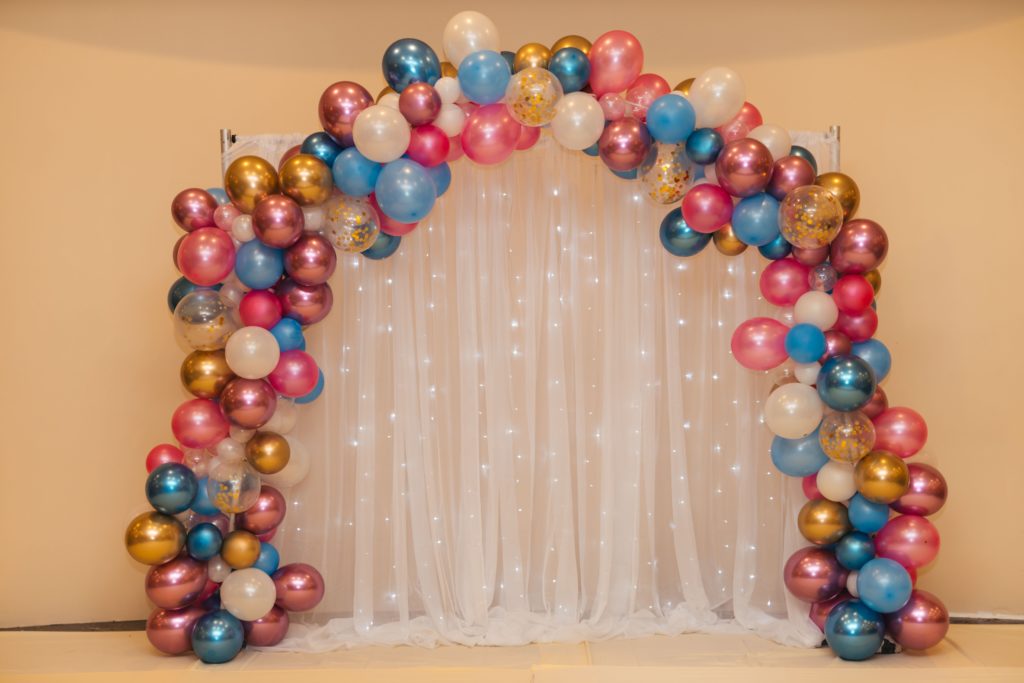 Wedding balloon arch with gold, blue, and pink balloons and white tulle backdrop