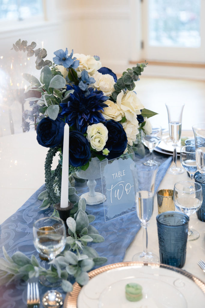 Wedding table set-up with blue flowers and signage and other decor.