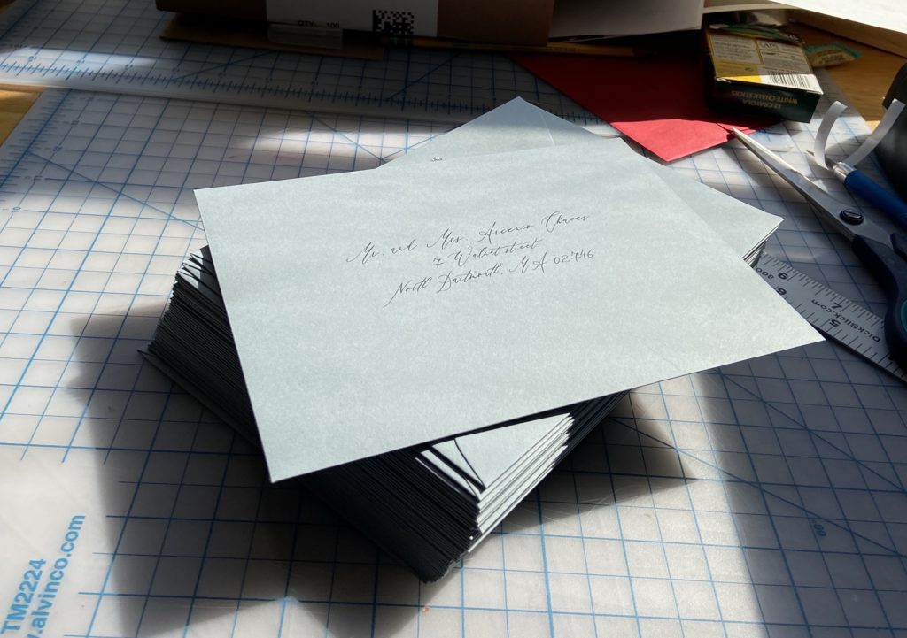 Stack of slate blue wedding invitations with printed calligraphy addresses.