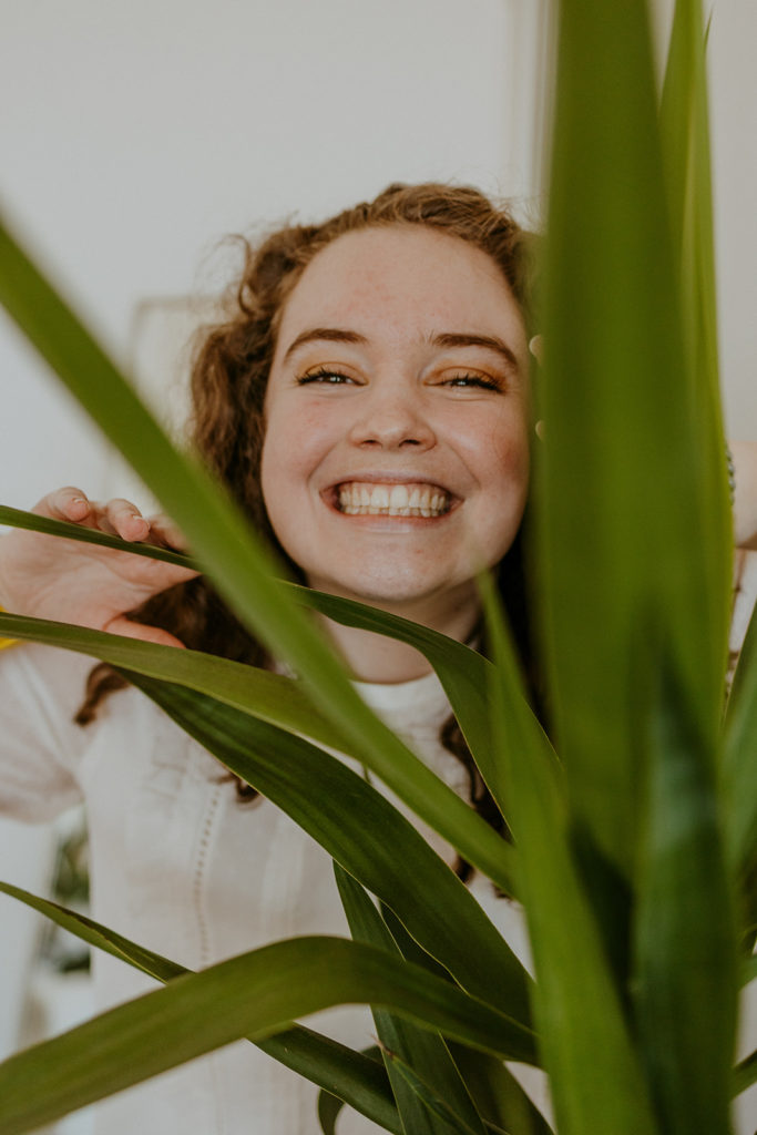CCB designer, Lauren, smiling from behind a plant.