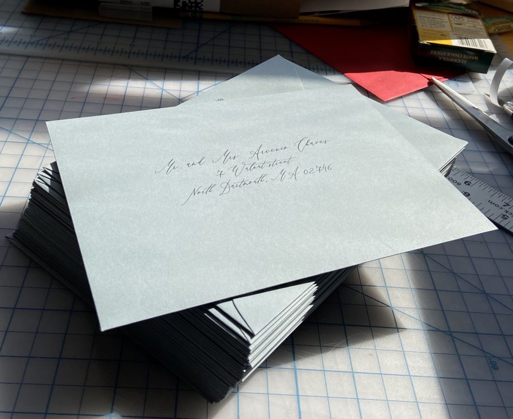 Stack of slate blue wedding envelopes with printed calligraphy addresses.