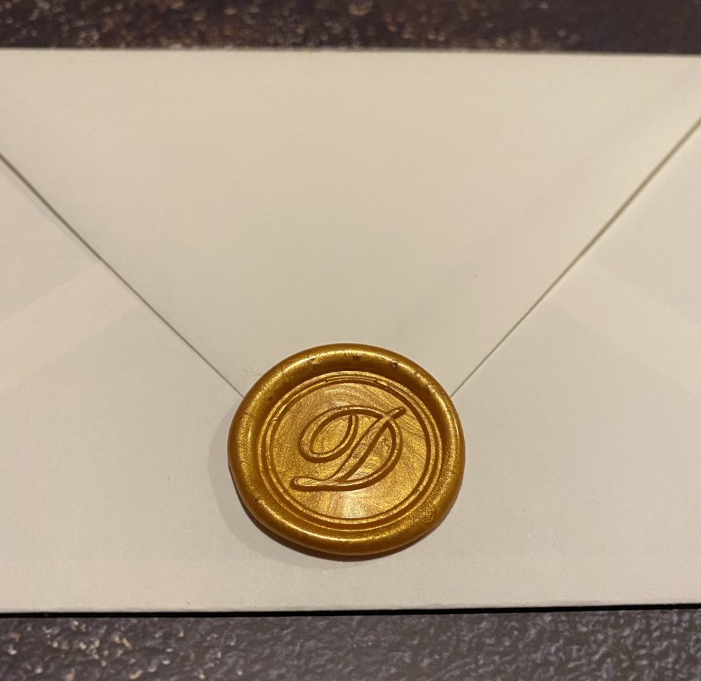 White inner envelope with a shiny gold wax seal with a custom D monogram.